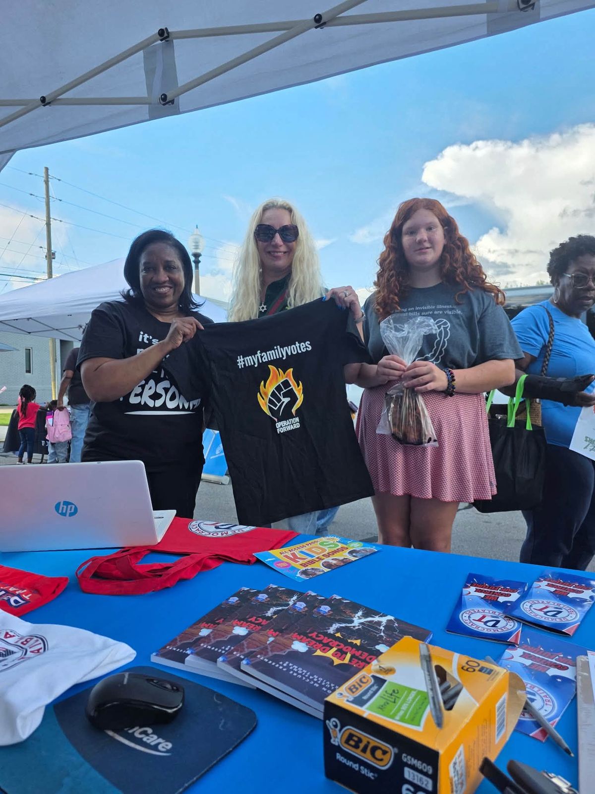 Volunteers holding up a #MyFamilyVotes shirt at a community event